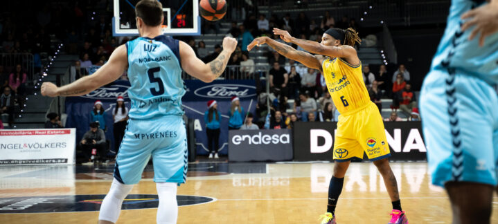 Jugador del Gran Canaria lanza el balón mientras el defensor observa en la cancha.