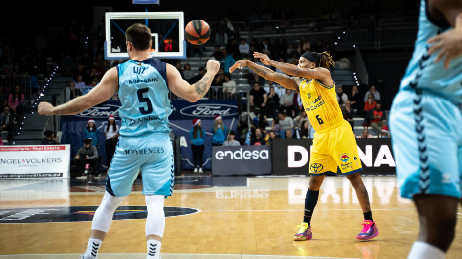 Jugador del Gran Canaria lanza el balón mientras el defensor observa en la cancha.
