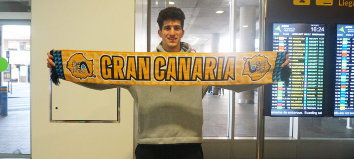 Jugador del CB Gran Canaria sostiene una bufanda del equipo en un aeropuerto.