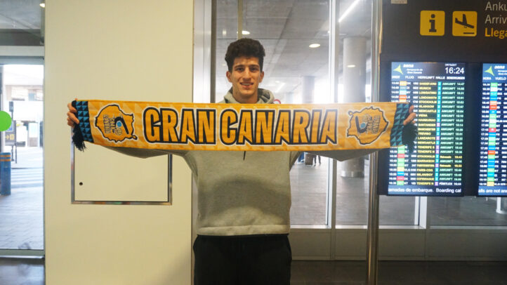 Jugador del CB Gran Canaria sostiene una bufanda del equipo en un aeropuerto.