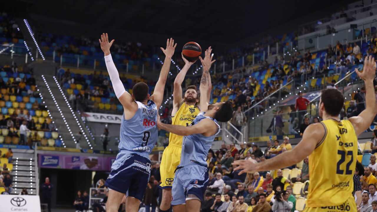 Jugadores del Gran Canaria en un salto para disputar el balón en un partido de baloncesto.