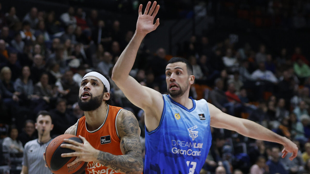 Jugadores de baloncesto en acción, uno atacando con el balón y el otro defendiendo.