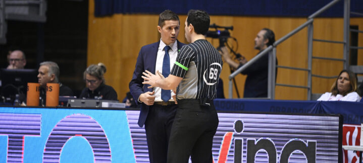 Entrenador conversando con un árbitro durante un partido de baloncesto.