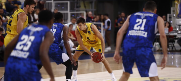 Jugadores en un partido de baloncesto, uno con balón en posición de pase.