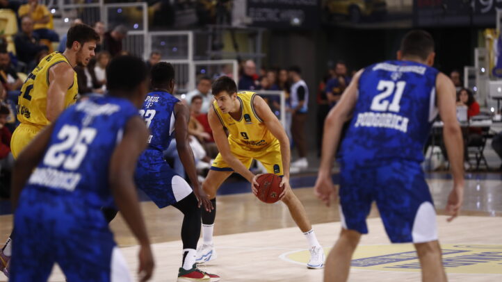 Jugadores en un partido de baloncesto, uno con balón en posición de pase.