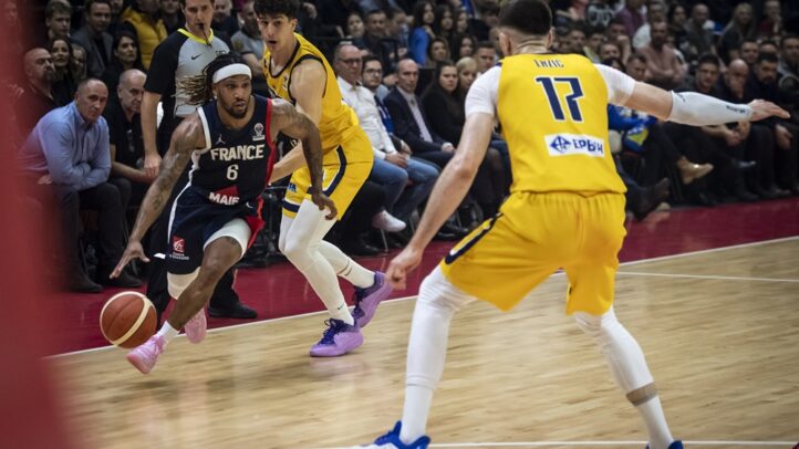 Baloncestista driblando con el balón, rodeado de otros jugadores en un partido.