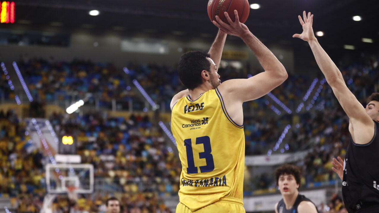 Jugador del Dreamland Gran Canaria lanzando el balón durante un partido, con público de fondo.