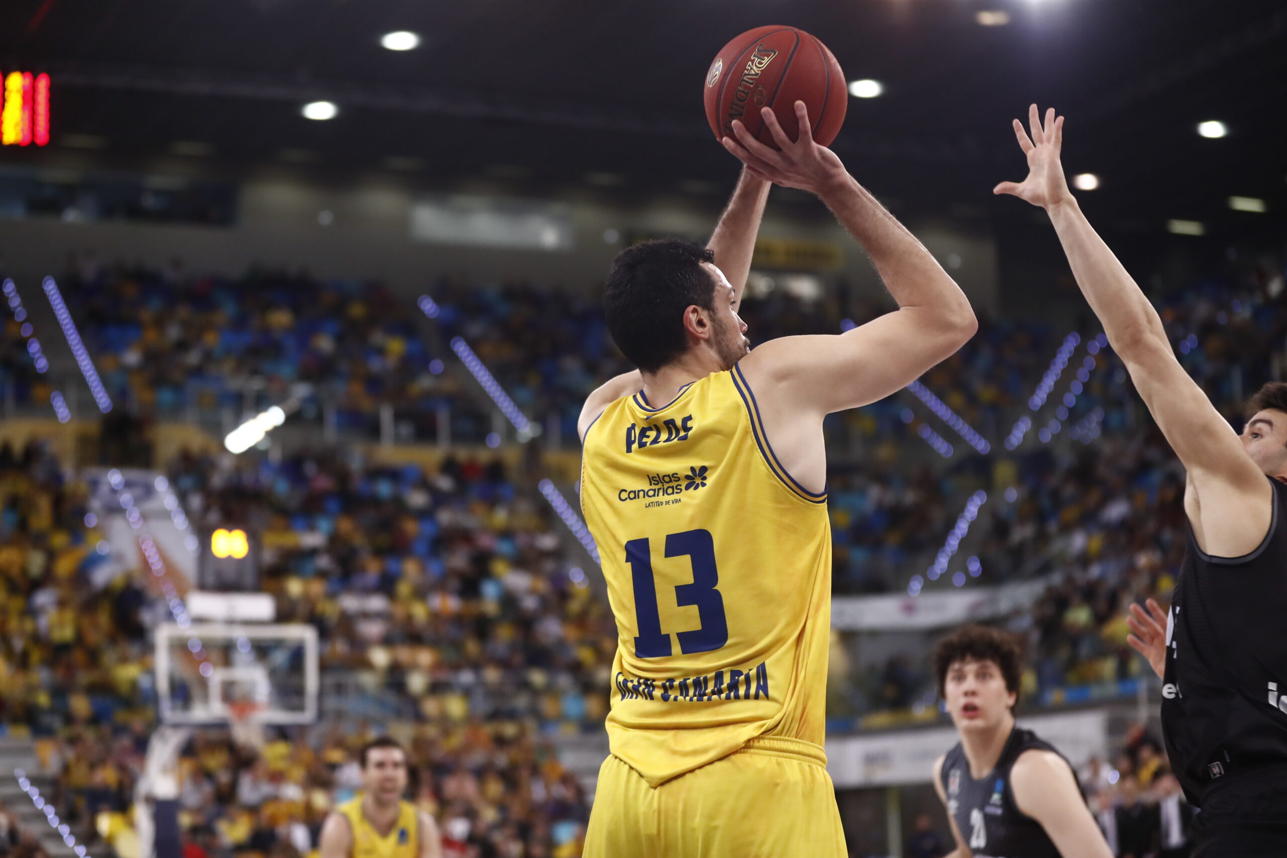 Jugador del Dreamland Gran Canaria lanzando el balón durante un partido, con público de fondo.