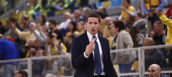 Entrenador Jaka Lakovic comunica de manera intensa durante un partido, con público al fondo.