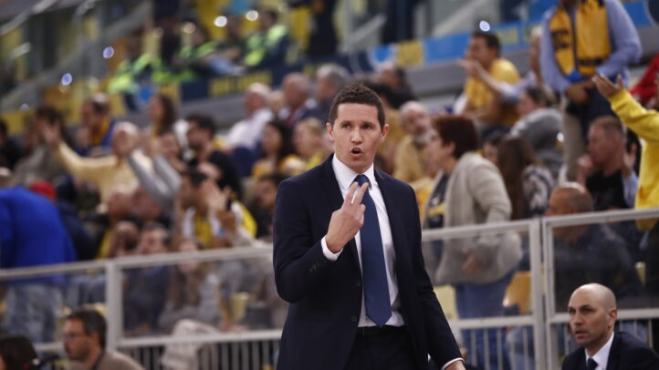 Entrenador Jaka Lakovic comunica de manera intensa durante un partido, con público al fondo.