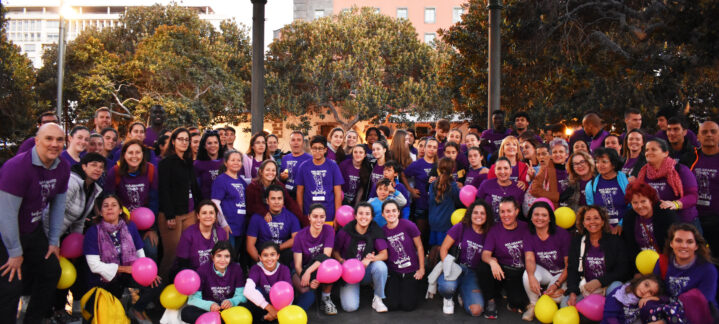 Grupo numeroso de personas vestidas de morado, celebrando el 8M con globos de colores.