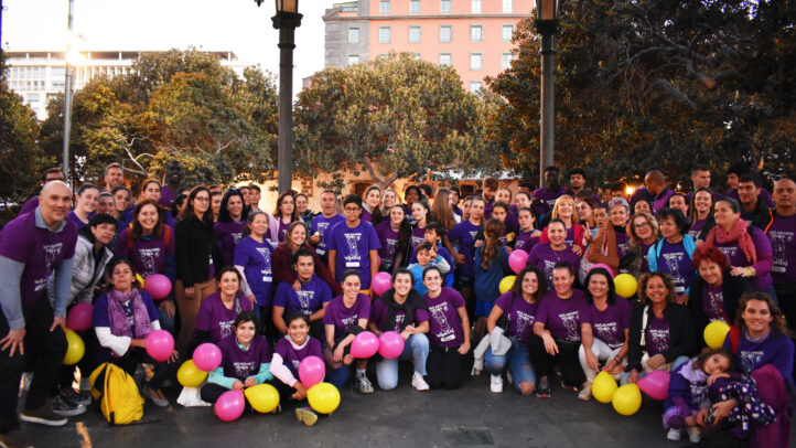 Grupo numeroso de personas vestidas de morado, celebrando el 8M con globos de colores.
