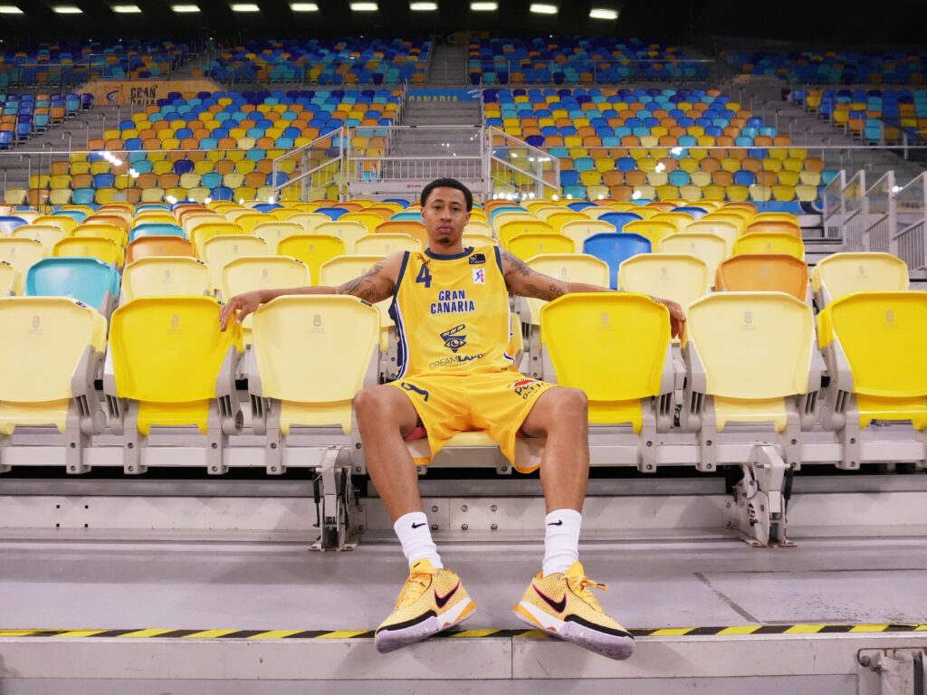 Jugador del CB Gran Canaria sentado en gradas vacías, luciendo uniforme amarillo.