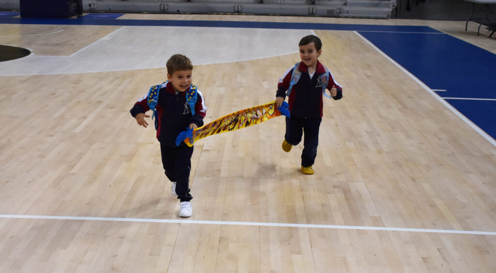 Dos niños corriendo en una cancha de baloncesto, sosteniendo un pañuelo juntos.