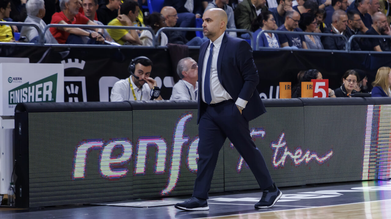 Entrenador caminando por la cancha durante un partido, observando el juego.