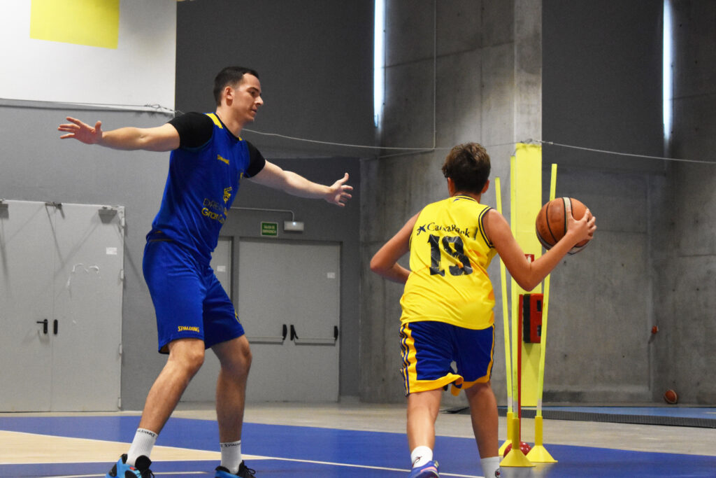 Entrenador guía a joven jugador de baloncesto durante una sesión técnica en la cancha.