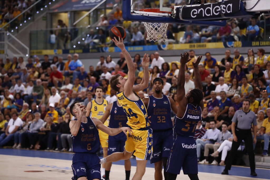 Jugador del Dreamland Gran Canaria lanza a canasta mientras es defendido por oponentes.