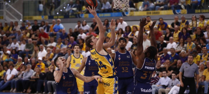 Jugador del Dreamland Gran Canaria lanza a canasta mientras es defendido por oponentes.