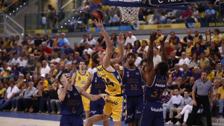 Jugador del Dreamland Gran Canaria lanza a canasta mientras es defendido por oponentes.