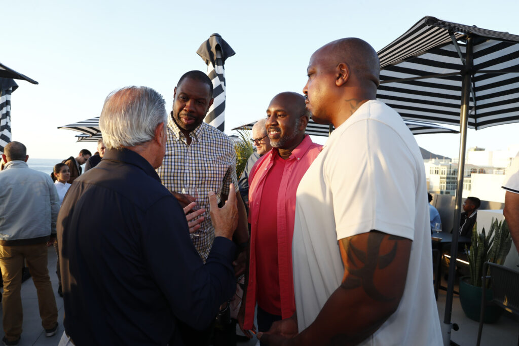 Cuatro hombres conversan al aire libre en un evento social en Las Canteras.