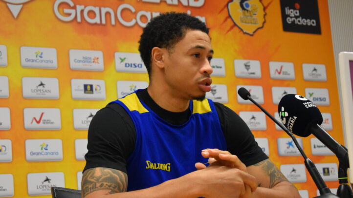 AJ Slaughter habla en rueda de prensa con el logo del equipo de fondo.