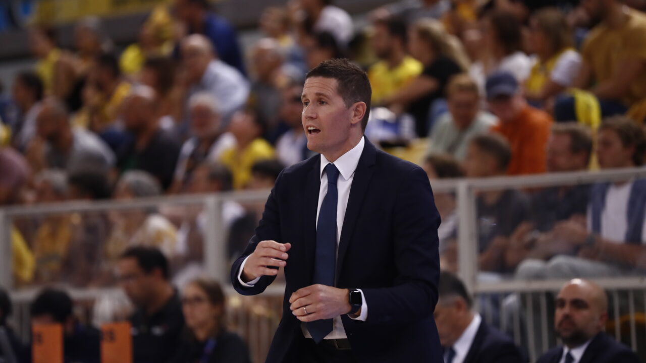 Entrenador Jaka Lakovic dirigiendo al equipo en una concurrida cancha de baloncesto.