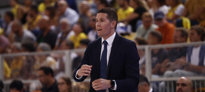 Entrenador Jaka Lakovic dirigiendo al equipo en una concurrida cancha de baloncesto.