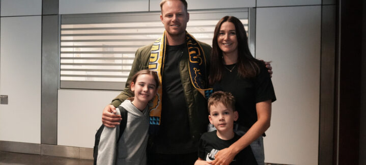 en la isla para su homenaje: ""Es genial estar en casa""","Brad Newley posando con su familia en el aeropuerto, envuelto en una bufanda del equipo.