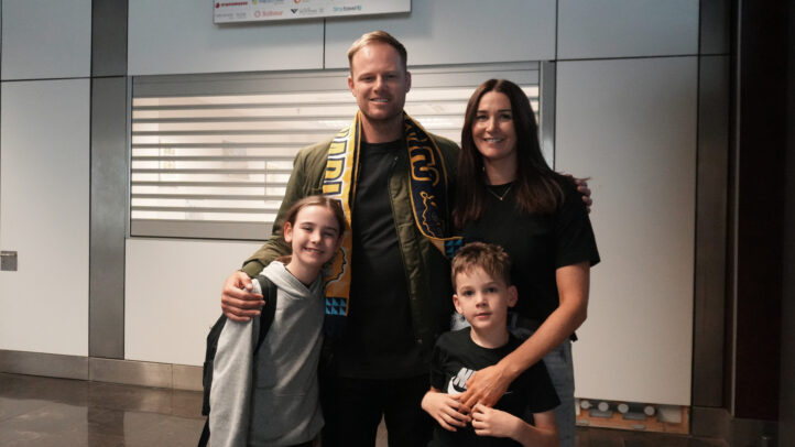 en la isla para su homenaje: ""Es genial estar en casa""","Brad Newley posando con su familia en el aeropuerto, envuelto en una bufanda del equipo.