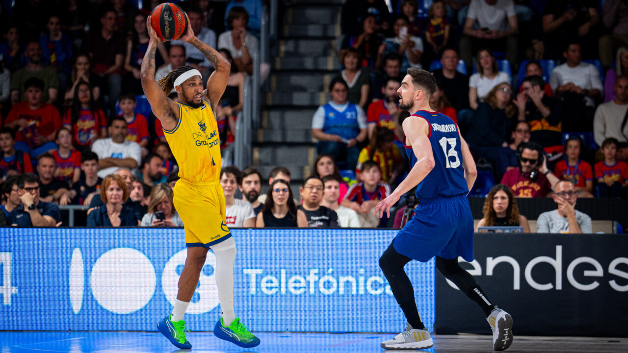 Jugadores de baloncesto en acción durante un partido en el Palau, con público en las gradas.