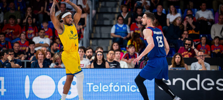 Jugadores de baloncesto en acción durante un partido en el Palau, con público en las gradas.