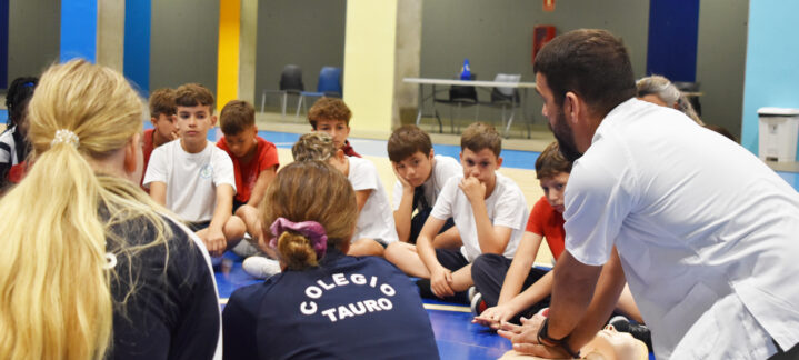 Grupo de jóvenes atentos a una demostración de primeros auxilios durante un entrenamiento.