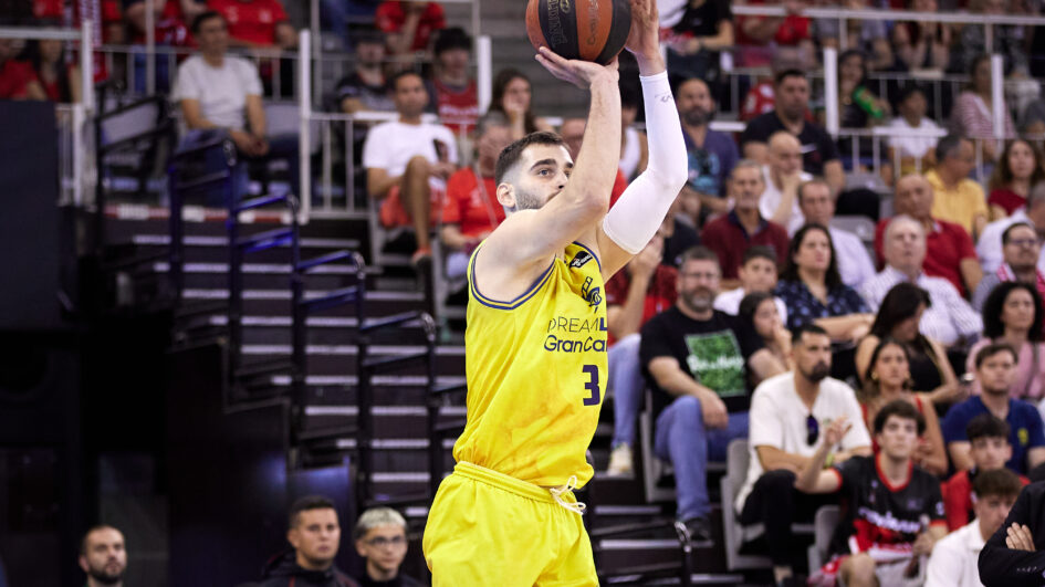 Jugador del CB Gran Canaria lanzando a canasta durante un partido, con público en las gradas.
