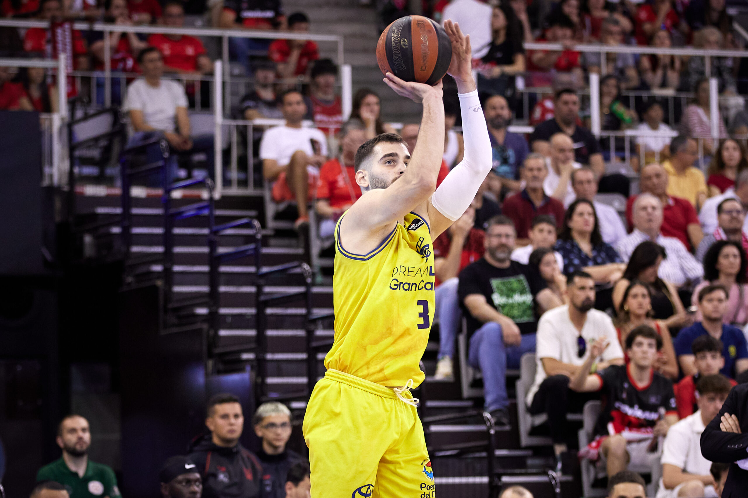 Jugador del CB Gran Canaria lanzando a canasta durante un partido, con público en las gradas.
