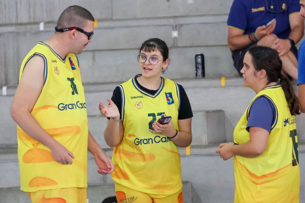 Tres jóvenes conversan en la cancha, vistiendo camisetas amarillas del CB Gran Canaria.