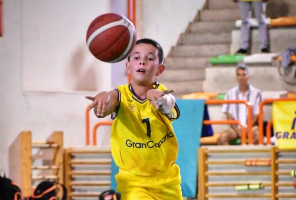 Niño en uniforme de baloncesto amarillo lanza un balón durante un partido.