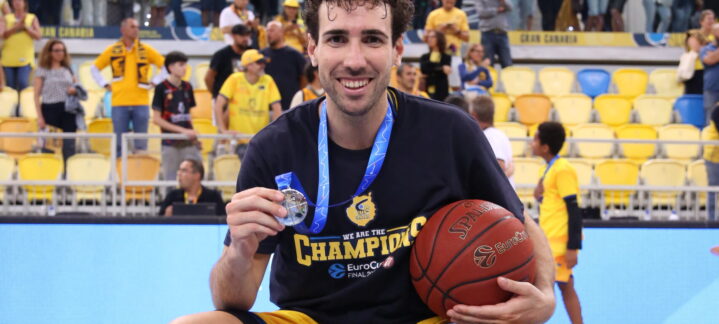 Jugador de baloncesto sosteniendo una medalla y un balón, celebrando en la pista.