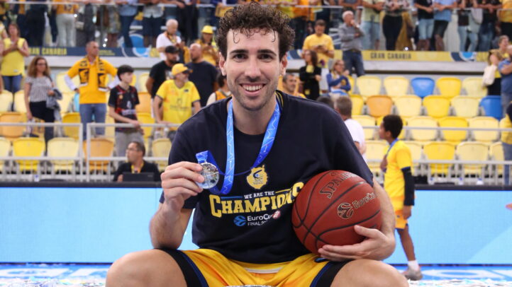 Jugador de baloncesto sosteniendo una medalla y un balón, celebrando en la pista.