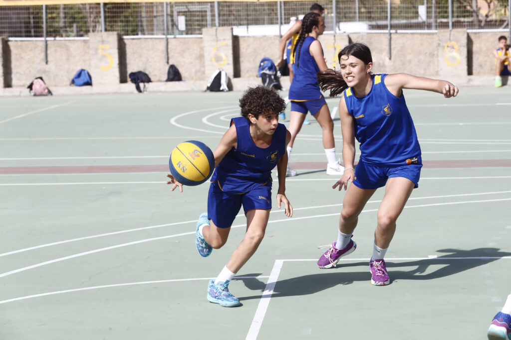 Niños y niñas juegan al baloncesto en una pista durante un evento escolar.