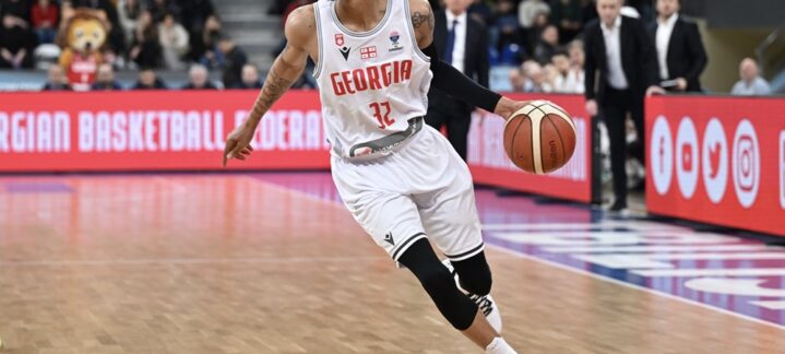 Jugador de baloncesto con camiseta blanca de Georgia driblando un balón en la cancha.