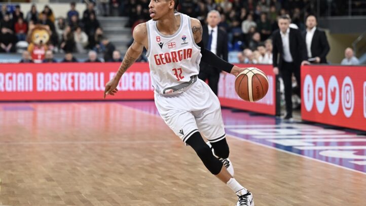 Jugador de baloncesto con camiseta blanca de Georgia driblando un balón en la cancha.