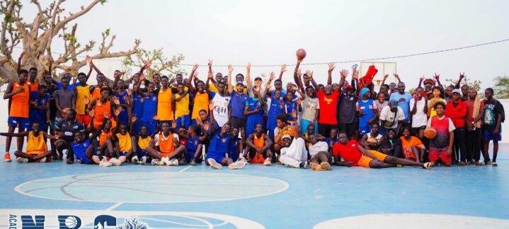 Grupo diverso de jugadores y entrenadores de baloncesto posando en una cancha al aire libre.