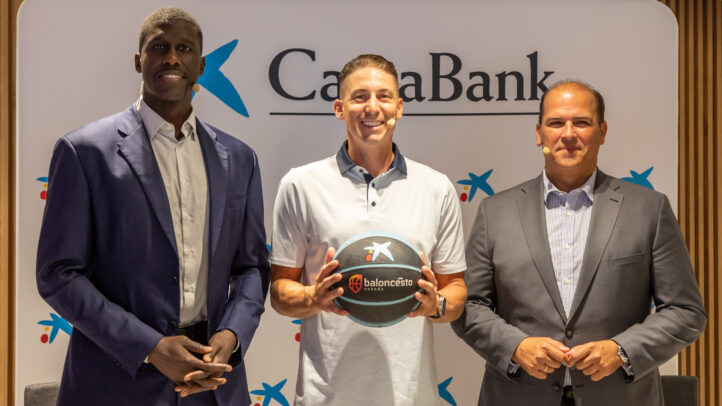 Tres hombres posan con un balón de baloncesto frente al logo de CaixaBank.