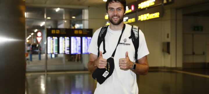 Jugador Mike Tobey en un aeropuerto, sonriendo y haciendo gesto de pulgar hacia arriba.