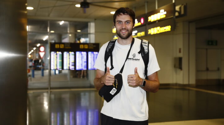 Jugador Mike Tobey en un aeropuerto, sonriendo y haciendo gesto de pulgar hacia arriba.