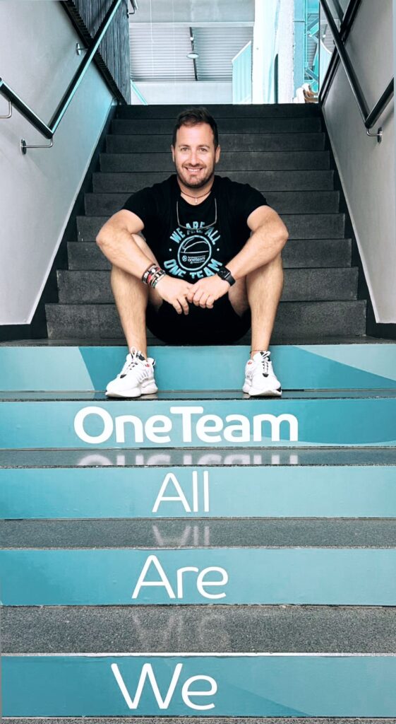 presente en el 14th One Team Annual Workshop 2024","Javier Choren sentado en escaleras con el lema ""One Team All Are We"".