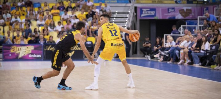 Jugadores en acción durante un partido de baloncesto, uno driblando y el otro defendiendo.