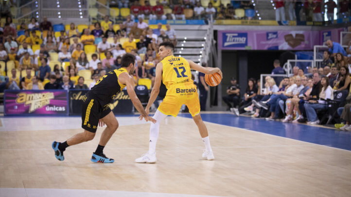 Jugadores en acción durante un partido de baloncesto, uno driblando y el otro defendiendo.
