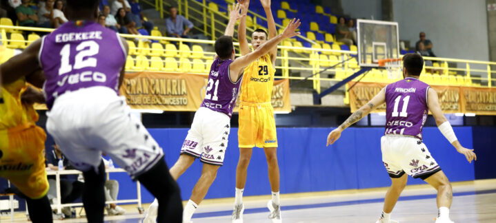Jugador lanzando un balón de baloncesto mientras es defendido por dos contrincantes.