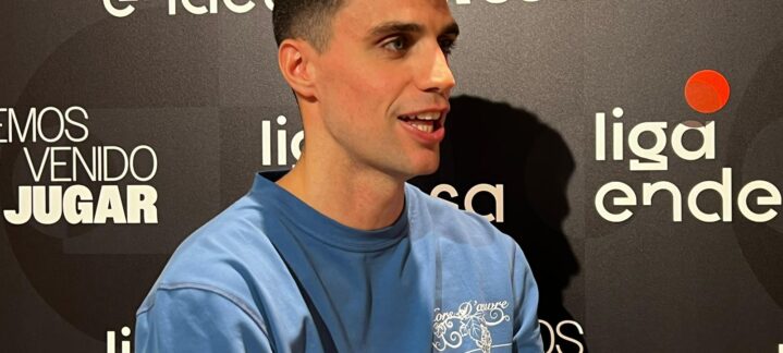 Carlos Alocén conversando en una rueda de prensa, con fondo del logo de la liga.